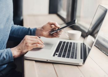 Man at a a laptop also looking at his phone