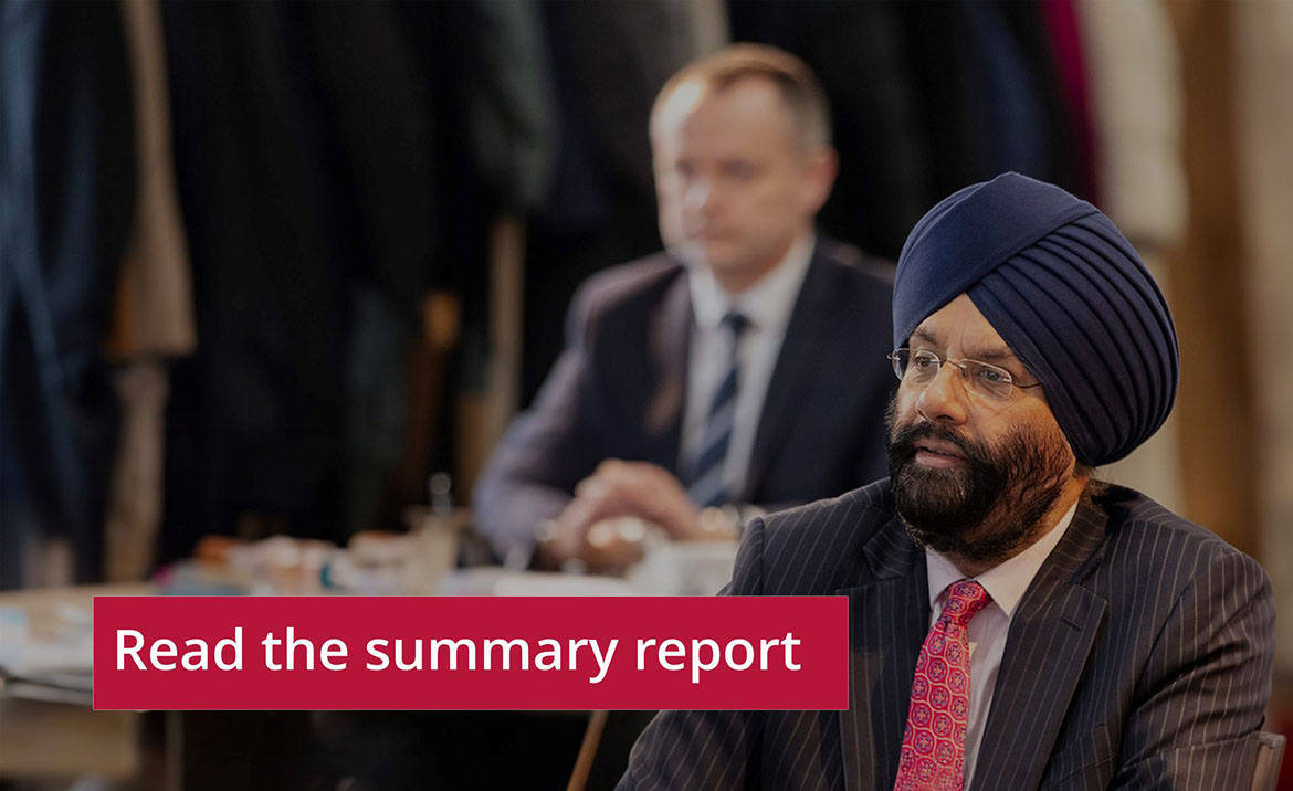 Person wearing a turban and glasses sitting thoughtfully at a conference table, with another individual in the background. A button reading 'Read the summary report' is displayed prominently in the foreground.